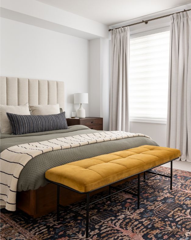 King sized bed in primary bedroom with layered bedding and yellow velvet bench